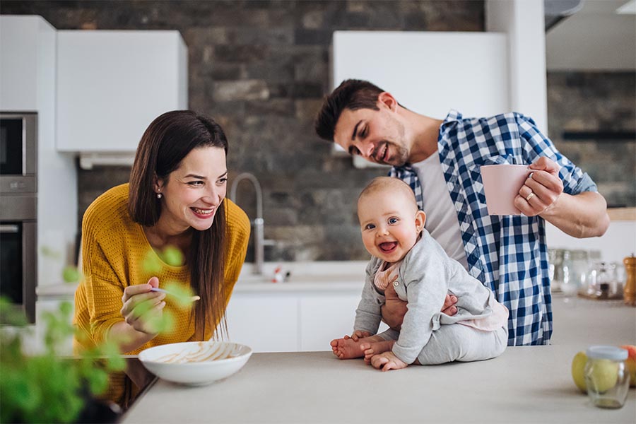 Personal Insurance - Young Family in Their Kitchen, Baby on the Counter, Parents Smiling Adoringly at Her